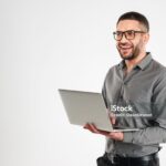 Photo of laughing businessman standing isolated over white background. Looking aside using laptop computer.