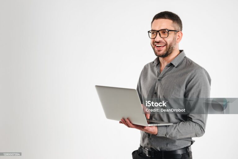 Photo of laughing businessman standing isolated over white background. Looking aside using laptop computer.
