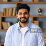 Headshot portrait of attractive confident indian Hispanic man with toothy smile looking at camera at modern library. Latin businessman posing in casual stylish look at home office.